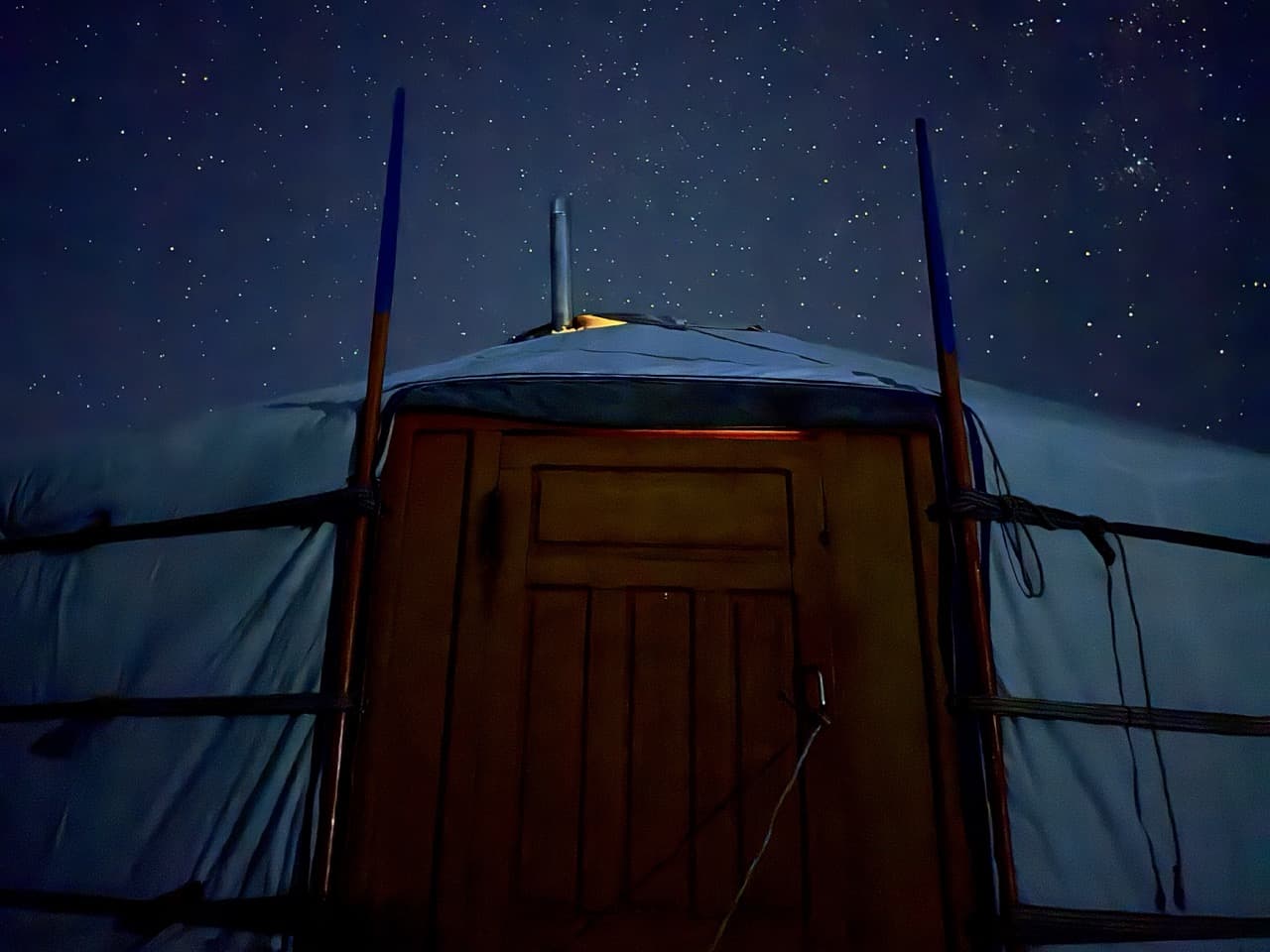 A ger at night under stars, light at the door and chimney.